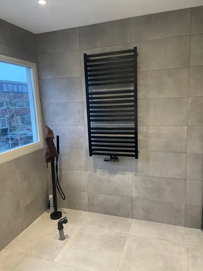 Badkamer in aanbouw met zwarte handdoekradiator en aangesloten doucheslang