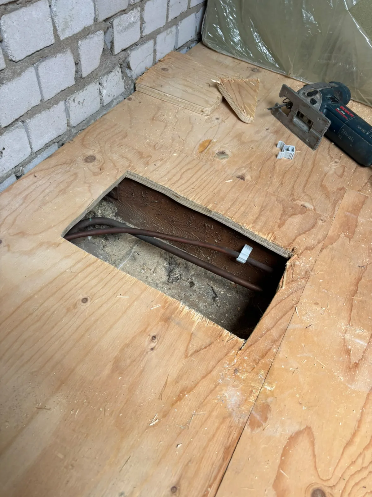 Houten vloer opengezaagd voor toegang tot onderliggende koperen leidingen, met zaagsel.