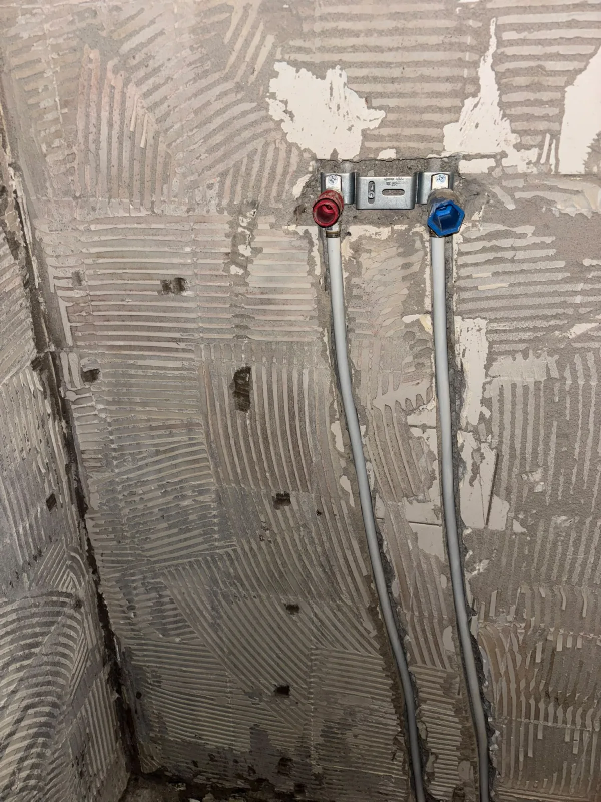 Muur met verwijderde tegels toont onderliggende leidingen voor warm en koud water.