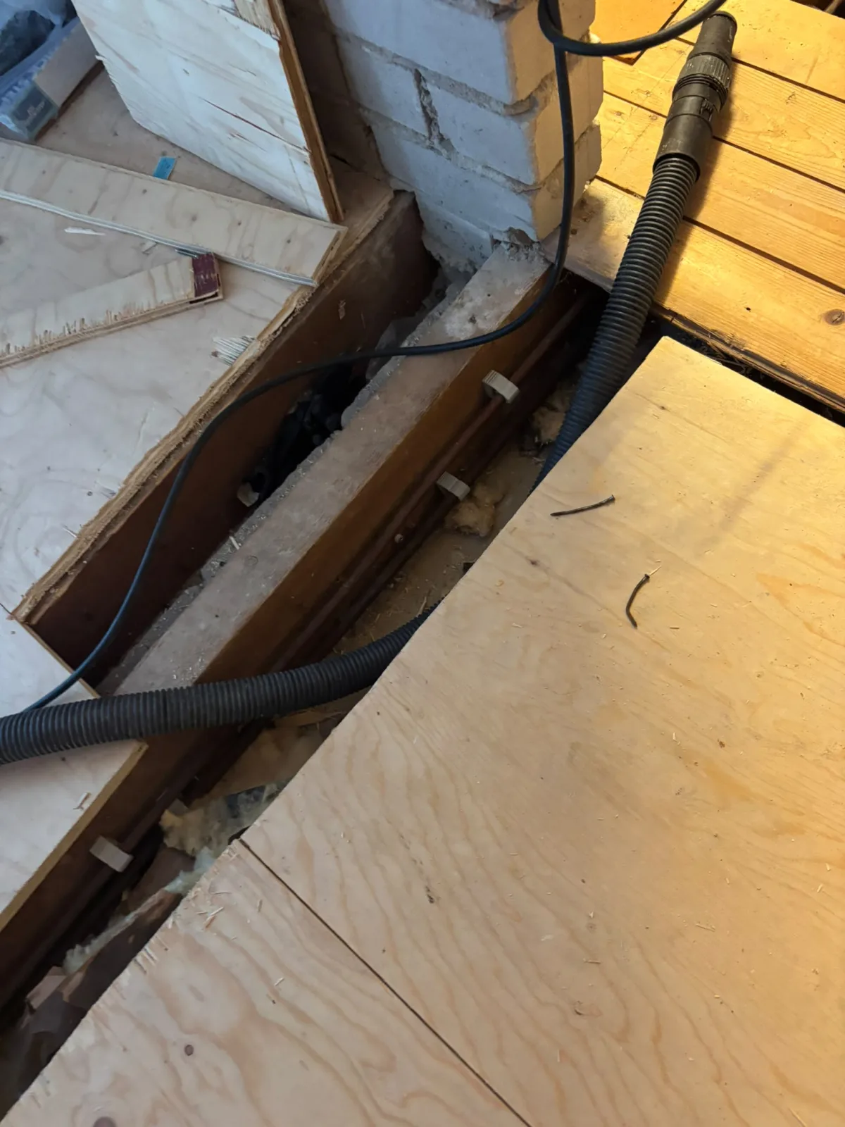 Opengebroken vloer met zichtbare leidingen en isolatie, houten planken eromheen.